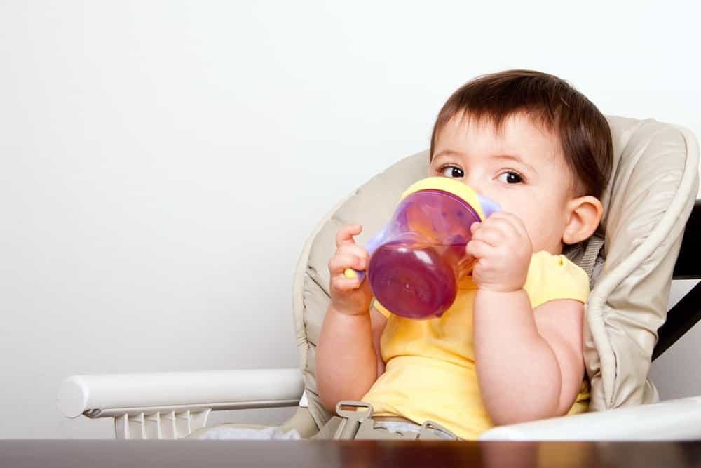 a baby in a high chair drinking out of a sippy cup
