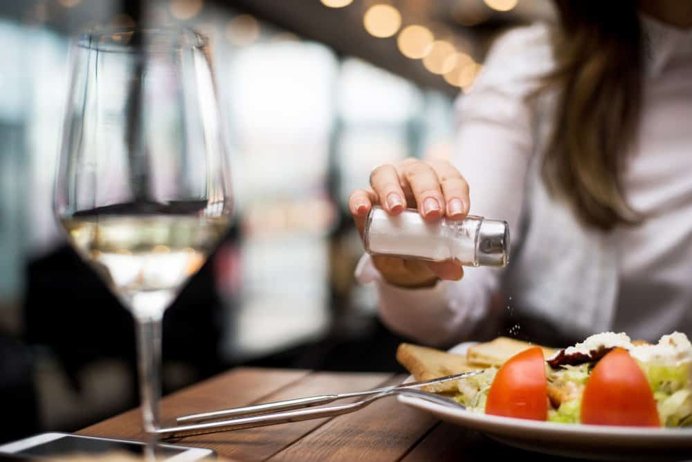 a woman adding salt to her dinner at a restaurant