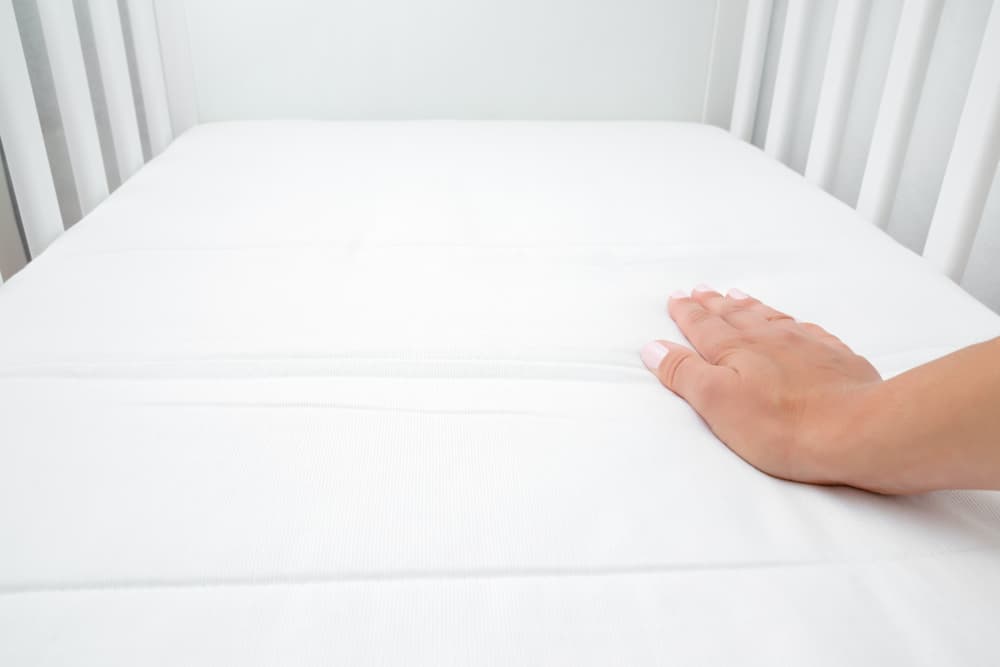 a woman’s hand pressing down on a crib mattress