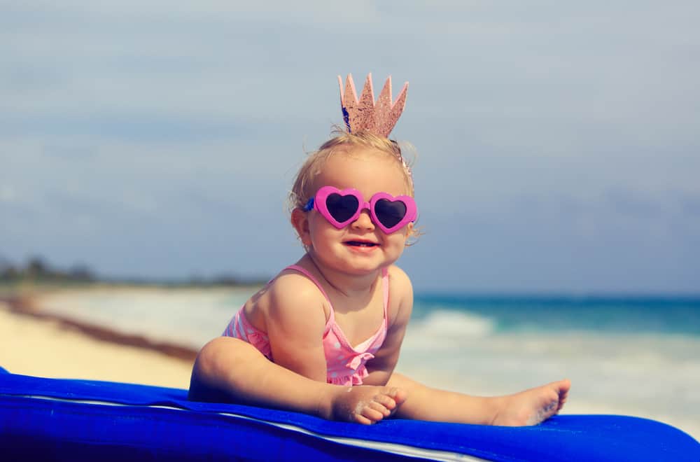 baby girl in a swimsuit and sunglasses on a surfboard