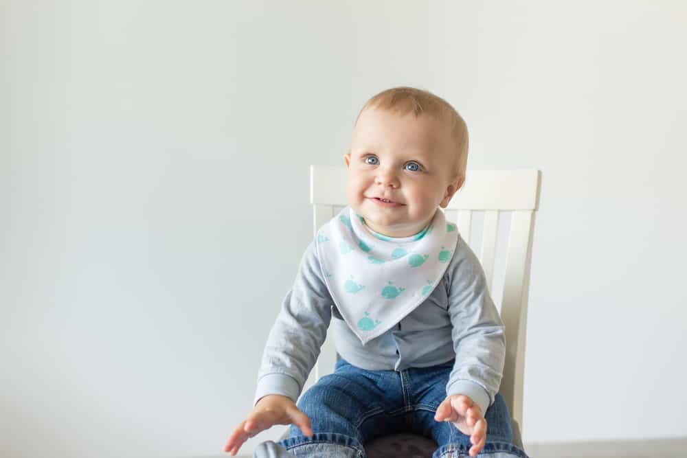 Baby in chair with his arms out, wearing a bib