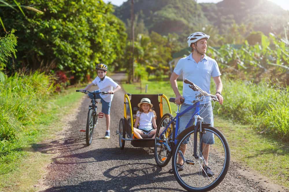 father and children biking through country roads with bike trailer