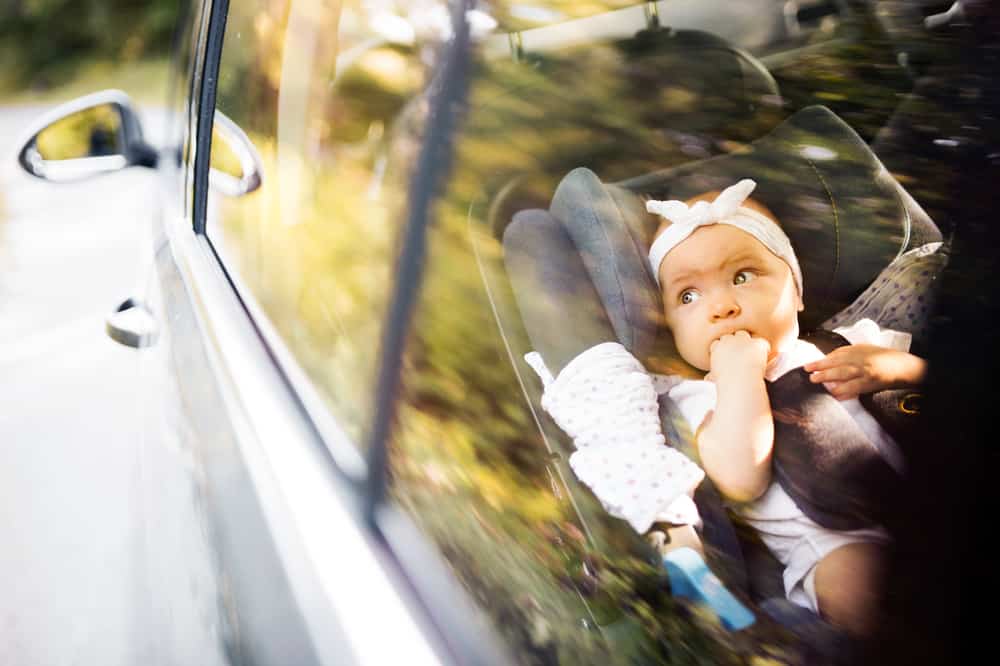 Baby fastened in car seat while looking out the window of the black car