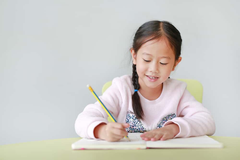 girl sat at table writing in notebook