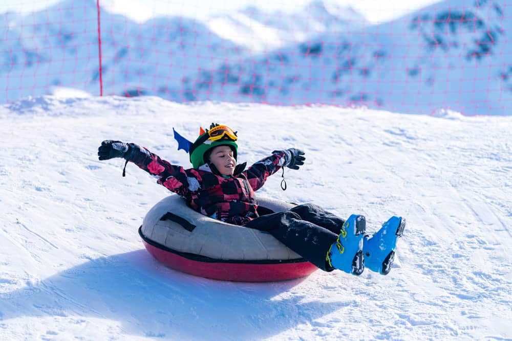 little boy in winter gear sledding on snow tube