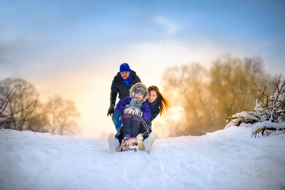 happy husband and wife sledding with their little girl