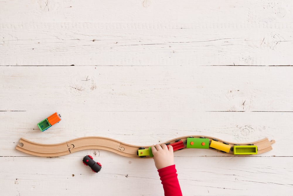 A child’s hand playing with wooden trains on wooden train tracks situated on a table