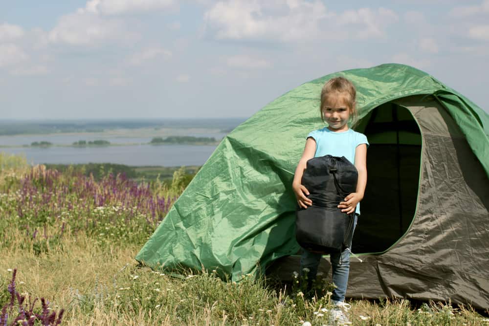 girl holding sleeping bag in front of tent