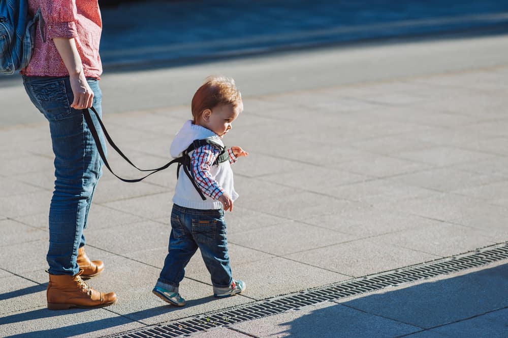 Mother walking with a child on a child leash on a sidewalk