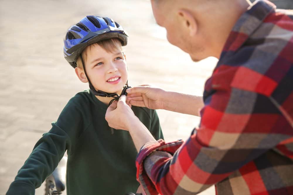 parent helping child put on bike helmet